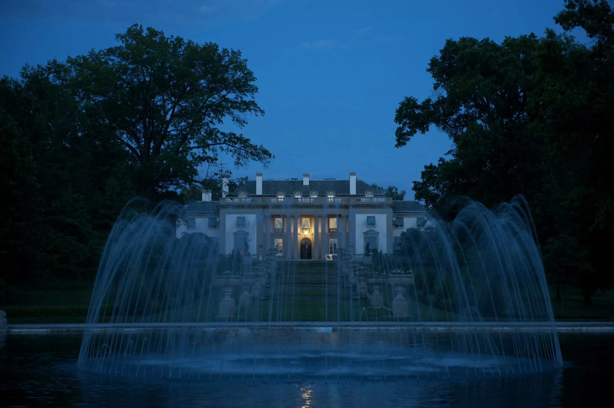 Nemours Estate at dusk, surrounded by trees, overlooking a fountain.